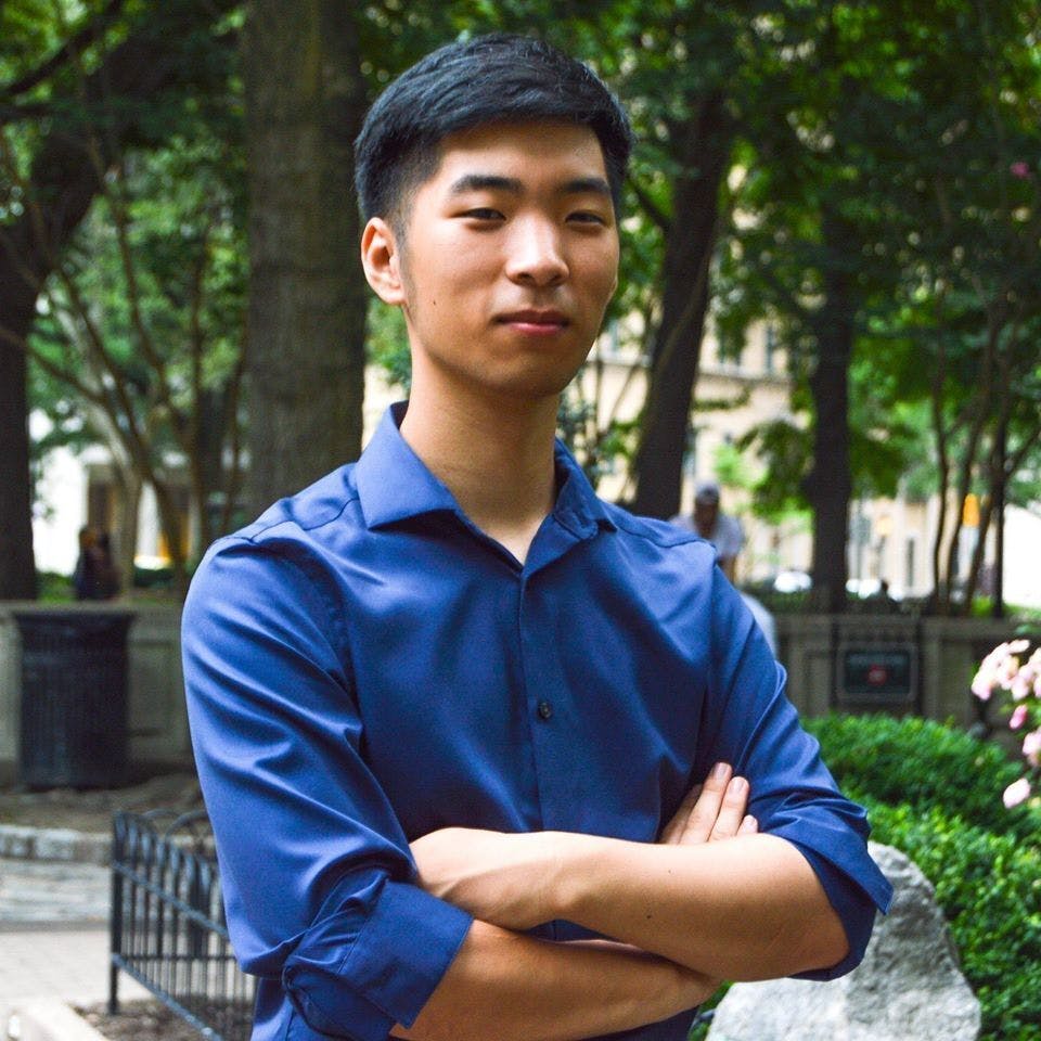 Headshot of Nathan, an Asian man wearing a blue shirt, with trees in the background.